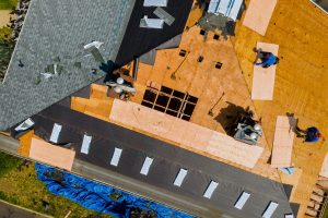 A roofer nailing shingles with air gun, replacing roof cover protection being applied, apartment development